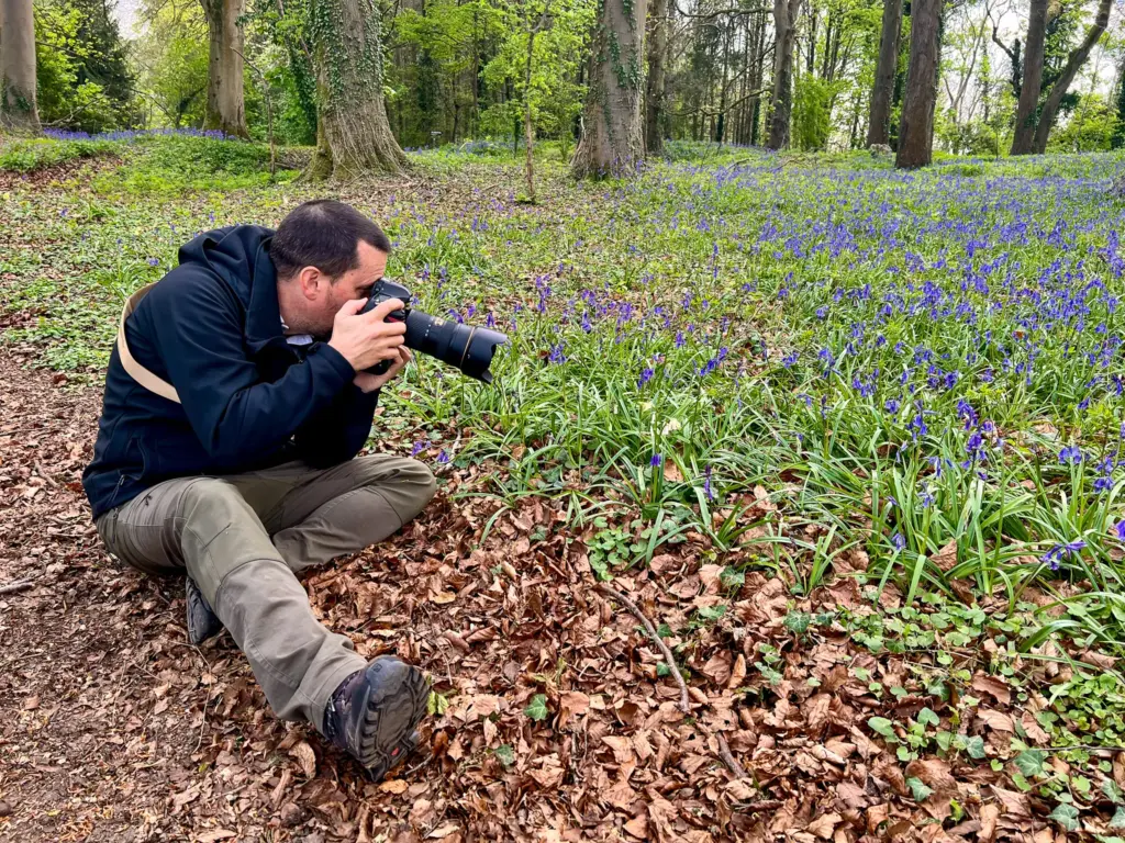 Glenn Bailey photographing bluebells in a wooded area at Dumbleton, Gloucestershire, surrounded by trees and vibrant spring flowers.