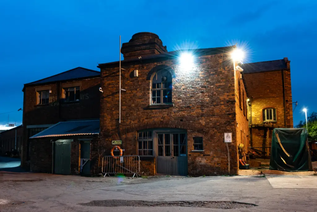 Illuminated brick industrial building at Gloucester Docks with security signage, life ring, and historical architecture at dusk.