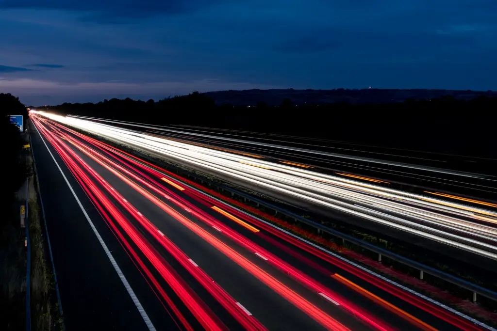 Highway light trails at night near M5 Junction 9, Tewkesbury, with red and white vehicle streaks and a dark sky.