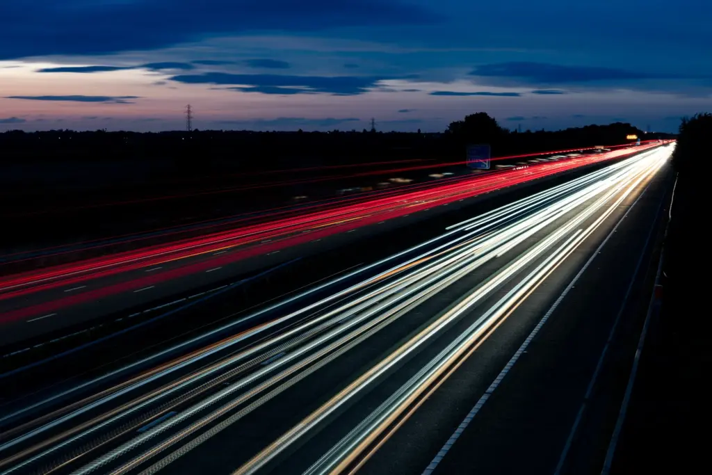 Nighttime long exposure of vehicle light trails on the M5 Junction 9 near Tewkesbury, showcasing red and white streaks of traffic.