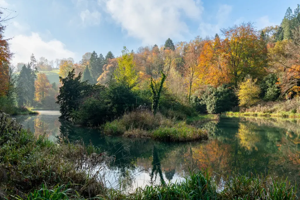 Autumn landscape at Miserden Estate near Stroud, featuring a calm pond surrounded by colorful trees and reflected in the water